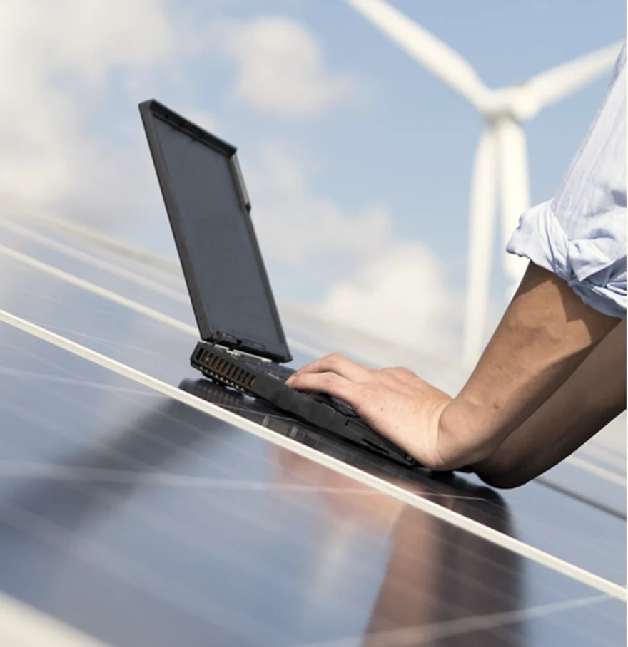 Laptop resting on a solar panel array with a wind turbine behind
